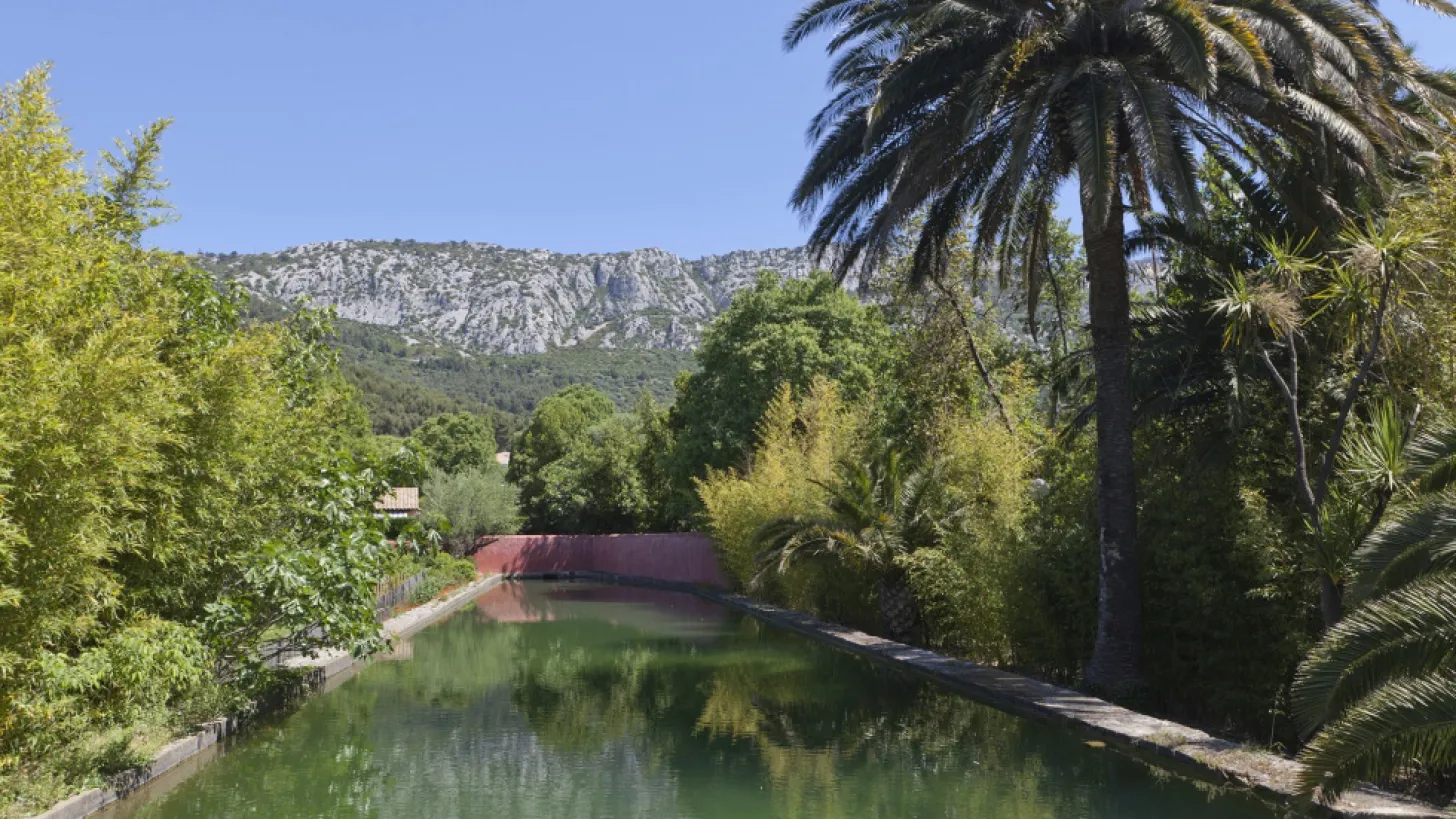 Jardin Remarquable de Baudouvin : vue sur un bassin avec une végétation luxuriante autour, au loin la colline et un beau ciel bleu.