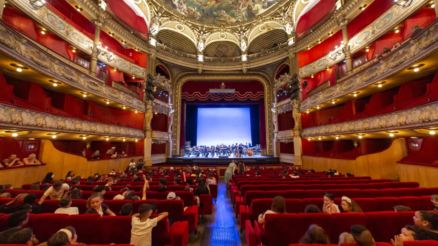 Opéra de Toulon : vue intérieur depuis la salle en rez de chaussée avec les fauteuils rouges, les balcons. Sur scène un concert de musique classique avec un public composé de scolaire.